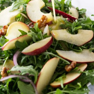 Salad bowl with arugula apple salad and a vinaigrette dressing being poured on.