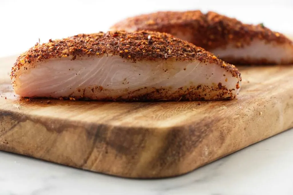 close up view of two uncooked portions of blackened halibut on a cutting board.