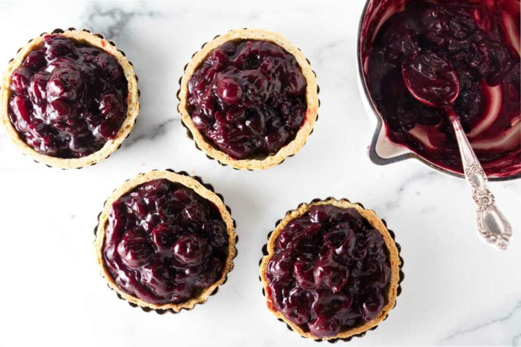 A pan of cherry filling spooned into four individual mini tarts.