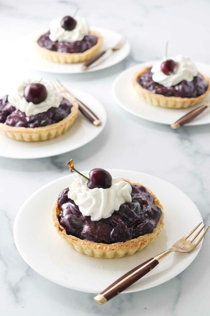Four servings of individual cherry tarts on serving plates.