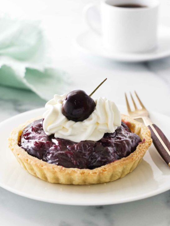 Mini cherry tart on a plate with a fork. Cup of coffee and napkin in the background.