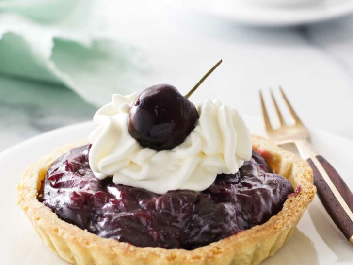 Mini cherry tart on a plate with a fork. Cup of coffee and napkin in the background.
