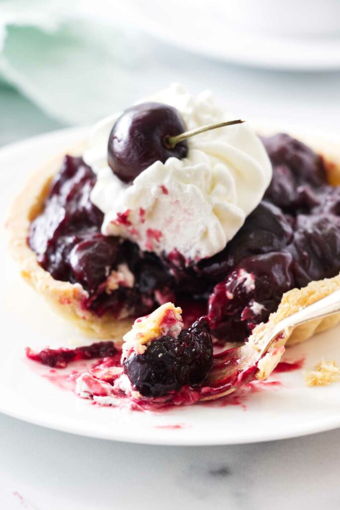 close up photo of a cherry tart and a bite of tart on a fork.