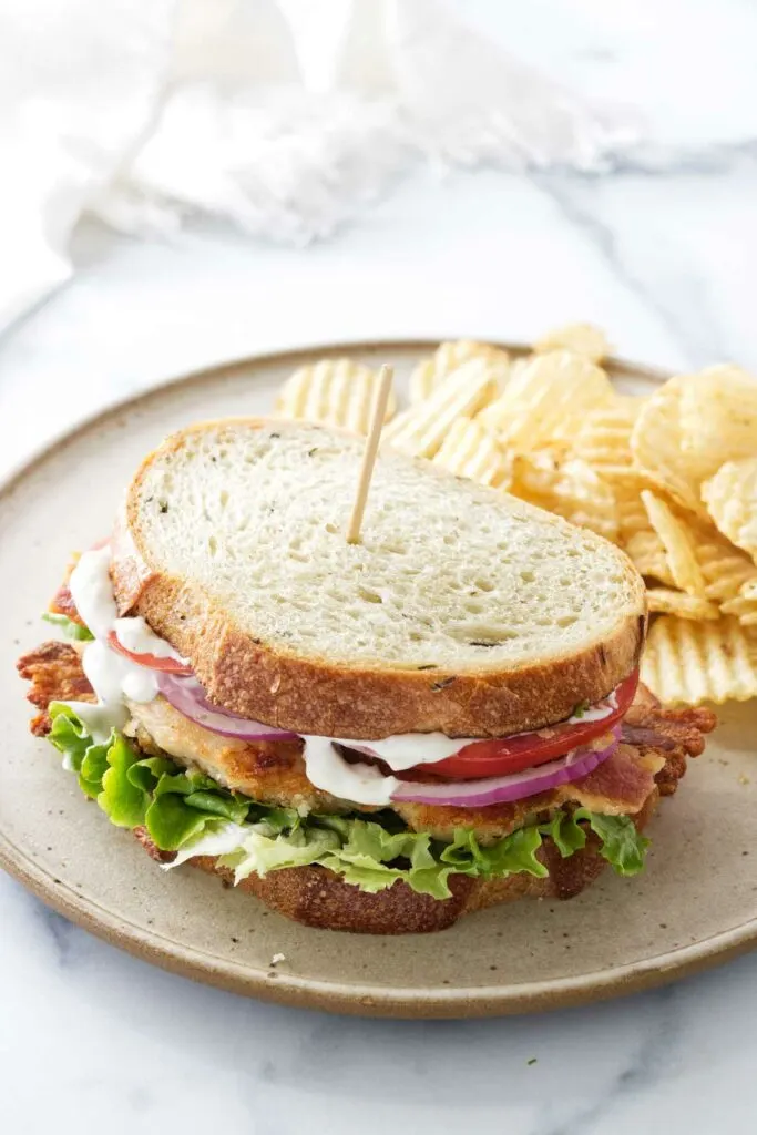 A chicken bacon ranch sandwich on a plate with a pile of potato chips.