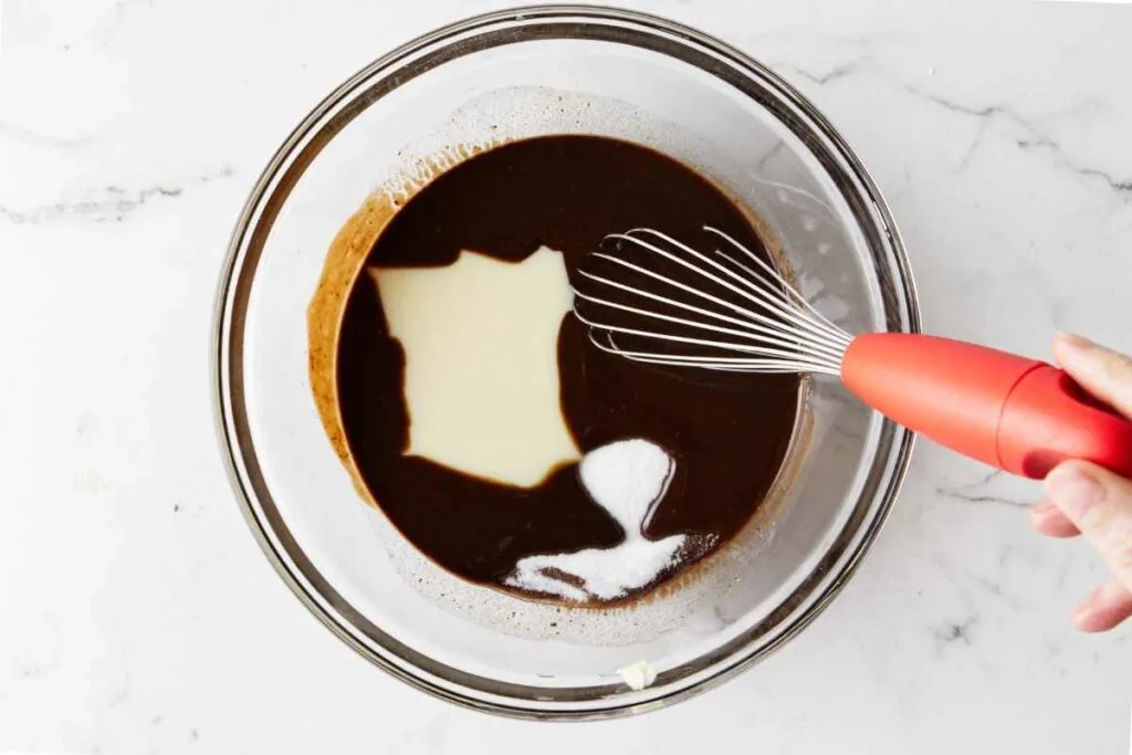 Whisking condensed milk and sugar into the chocolate mixture.