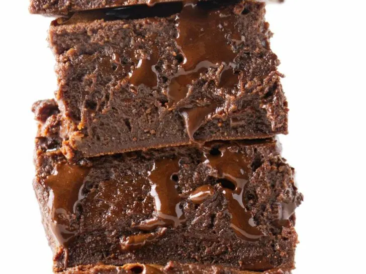 A stack of four condensed milk brownies with melted chocolate dripping out of them.