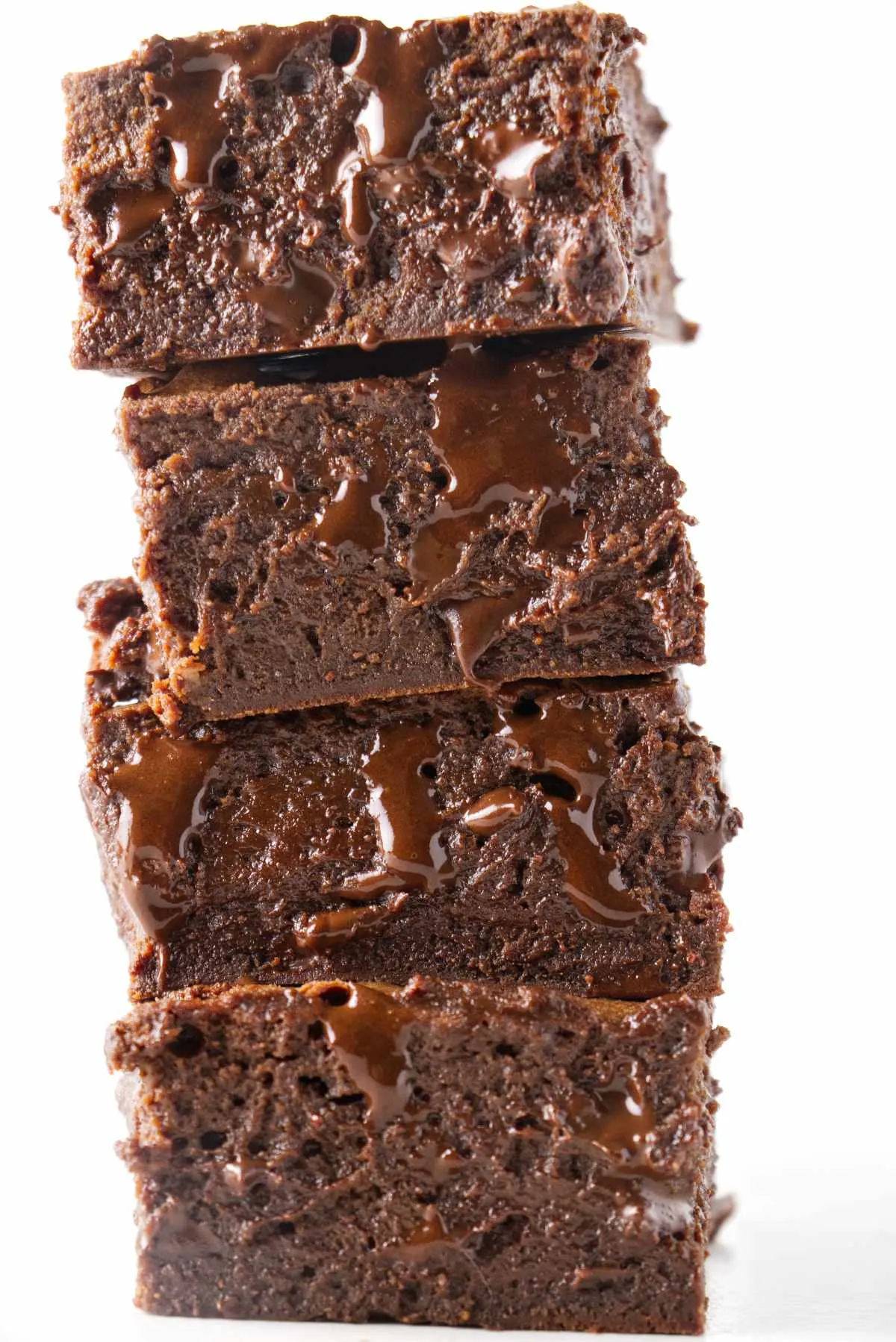 A stack of four condensed milk brownies with melted chocolate dripping out of them.