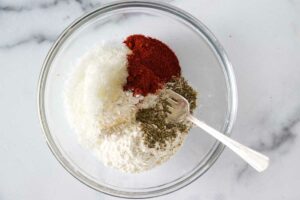 A small dish with grated cheese, paprika powder, Italian spices and flour.