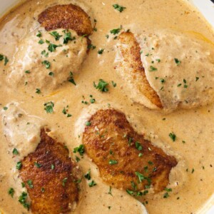 A pan of creamy paprika sauce and four chicken breasts. A spoon with sauce.