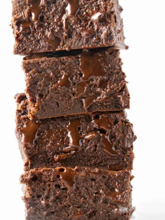 A stack of four condensed milk brownies with melted chocolate dripping out of them.