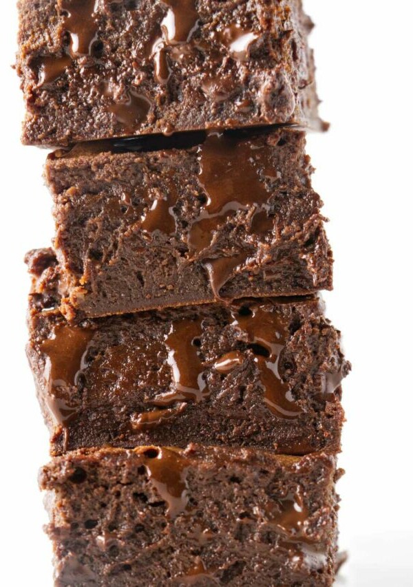 A stack of four condensed milk brownies with melted chocolate dripping out of them.