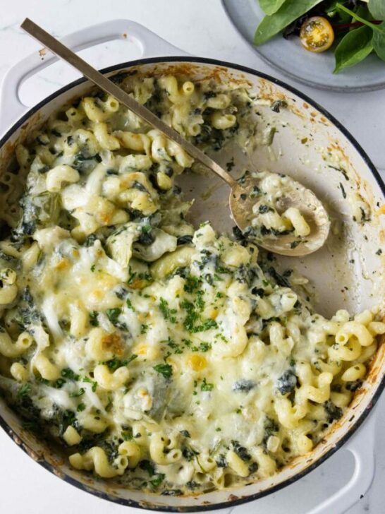 A spoon in a skillet filled with a pasta bake.