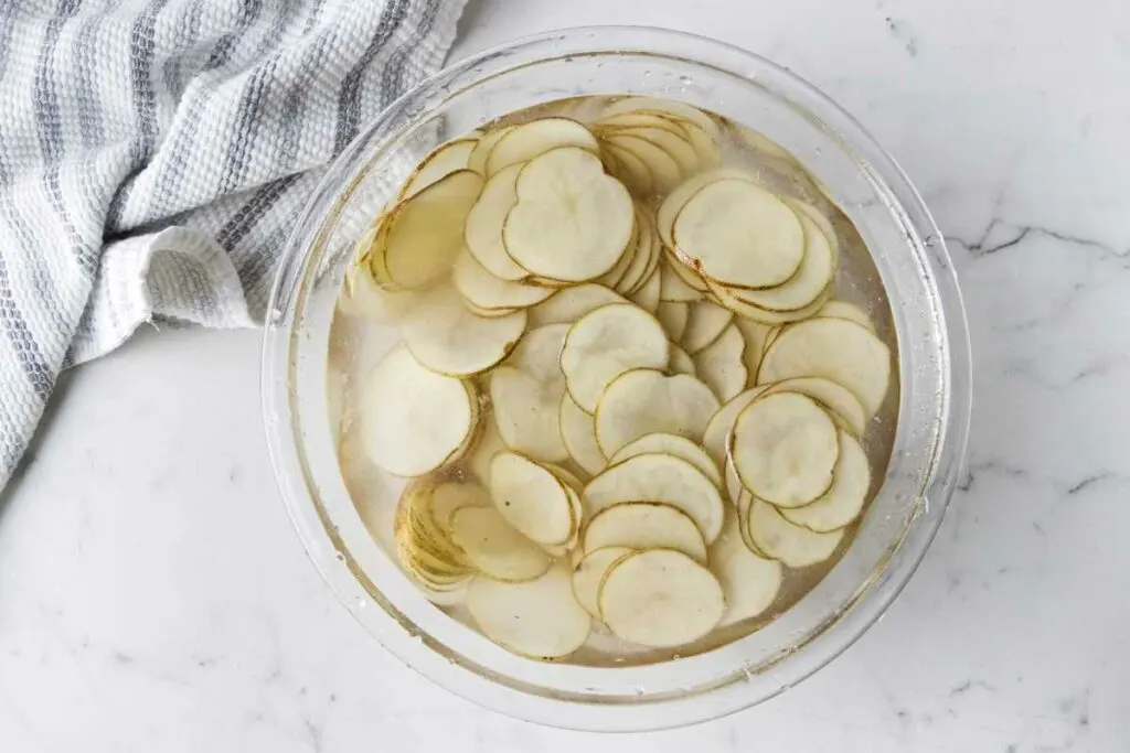 Adding potato slices to a bowl of cold water.