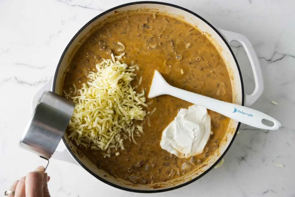 Stirring sour cream and cheese into the ground beef mixture.