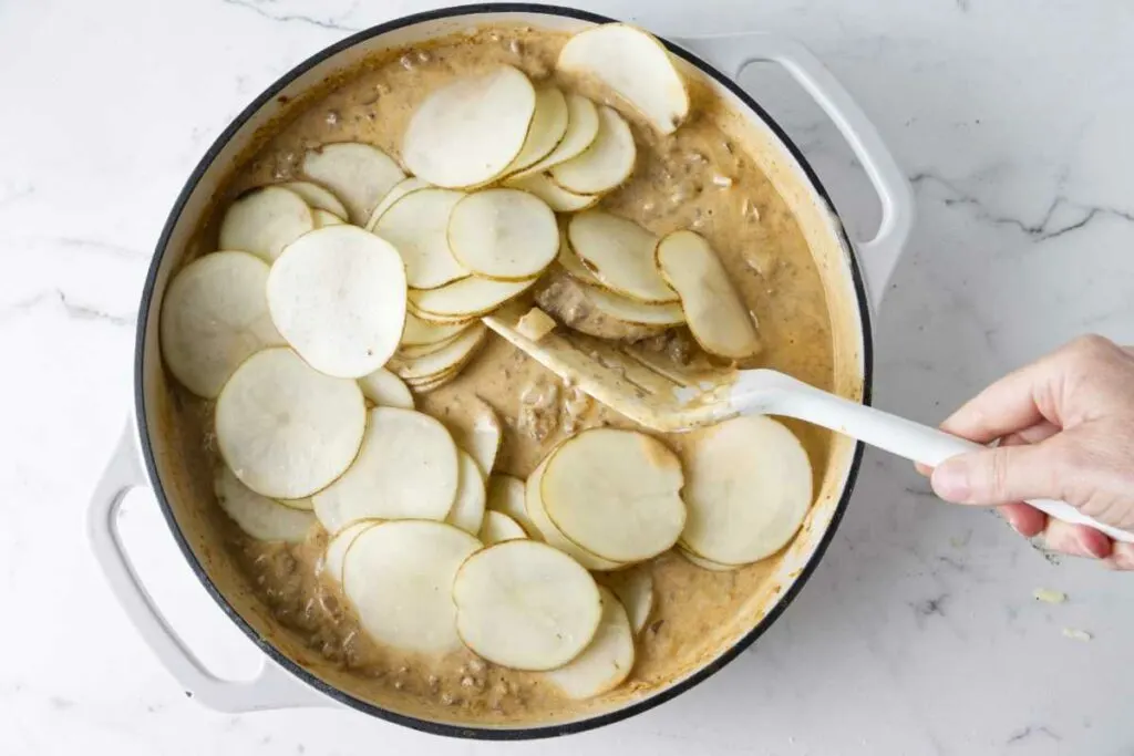 Mixing the potato slices into the ground beef casserole.