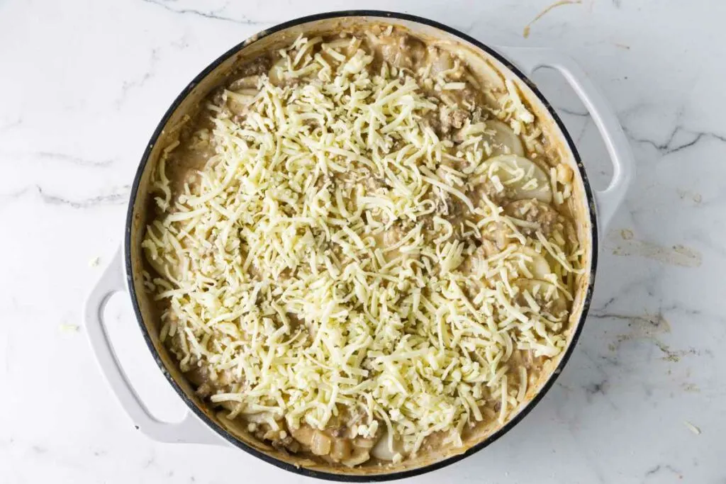 Adding shredded cheese to the top of the hamburger potato skillet.