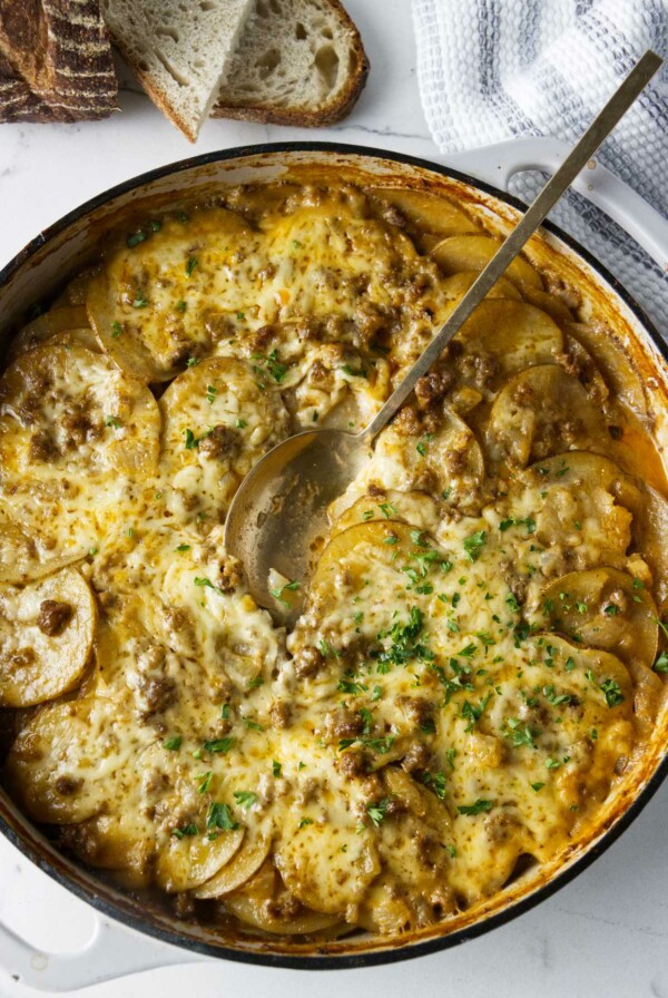 A serving spoon in a skillet of hamburger potato bake.