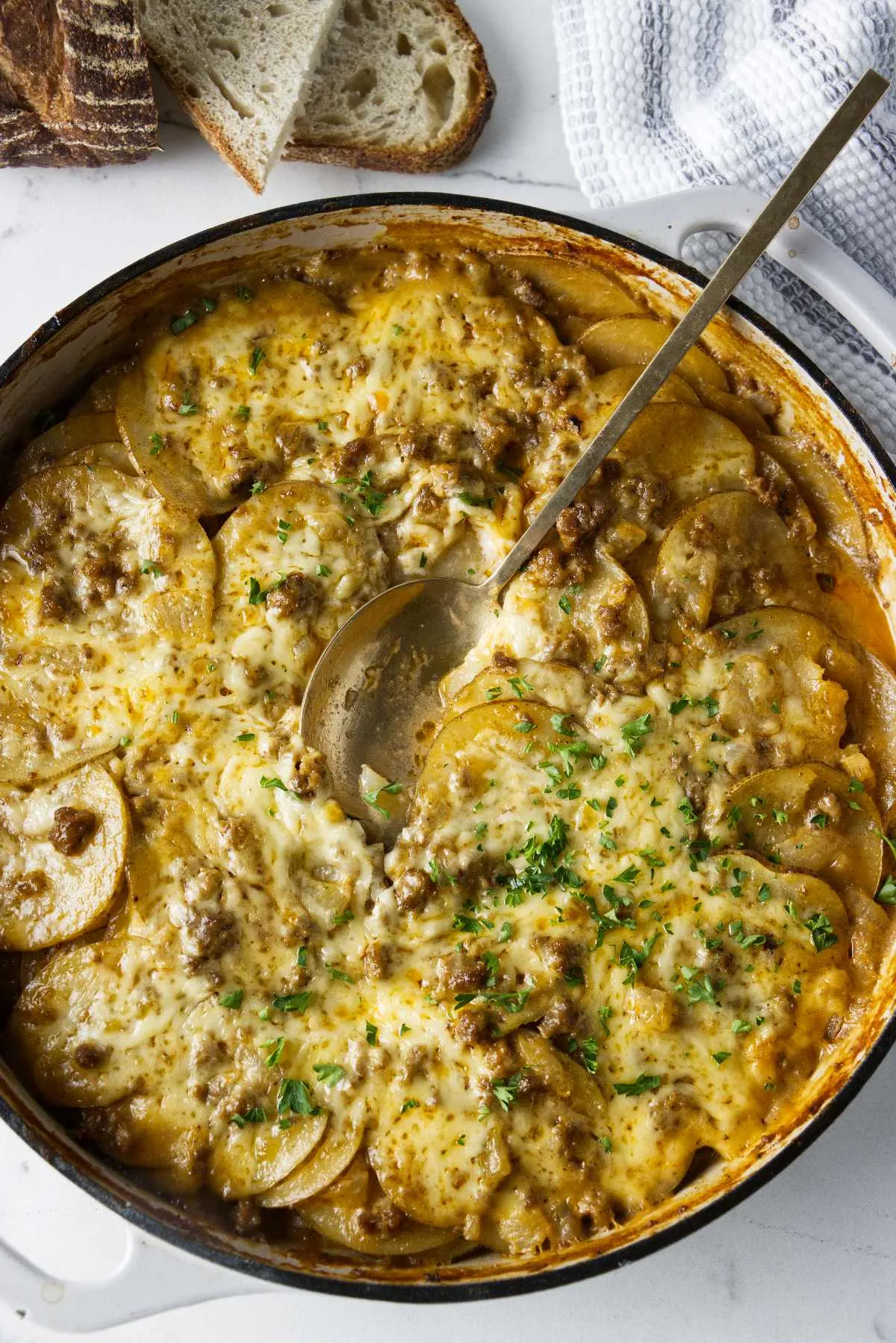 A serving spoon in a skillet of hamburger potato bake.