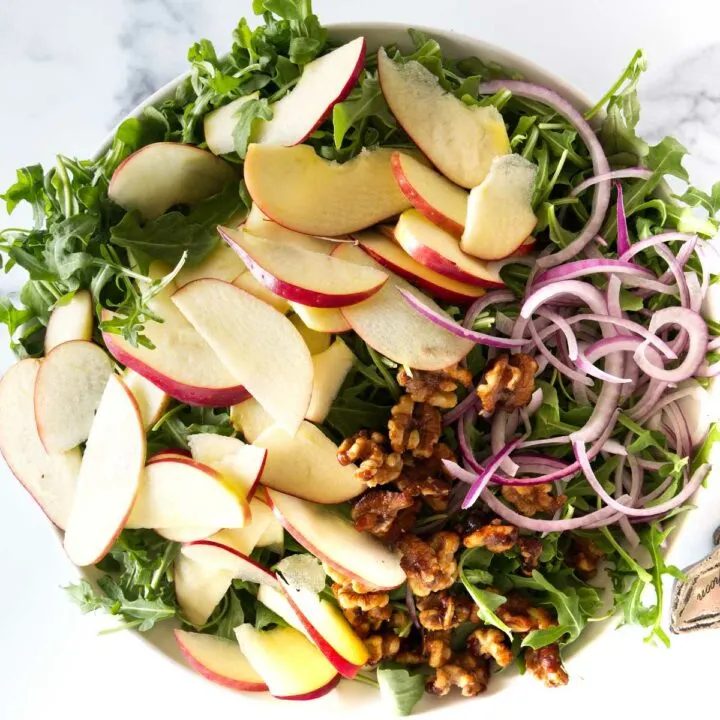Overhead view of arugula apple salad with walnuts and red onion slices, ready to be tossed.
