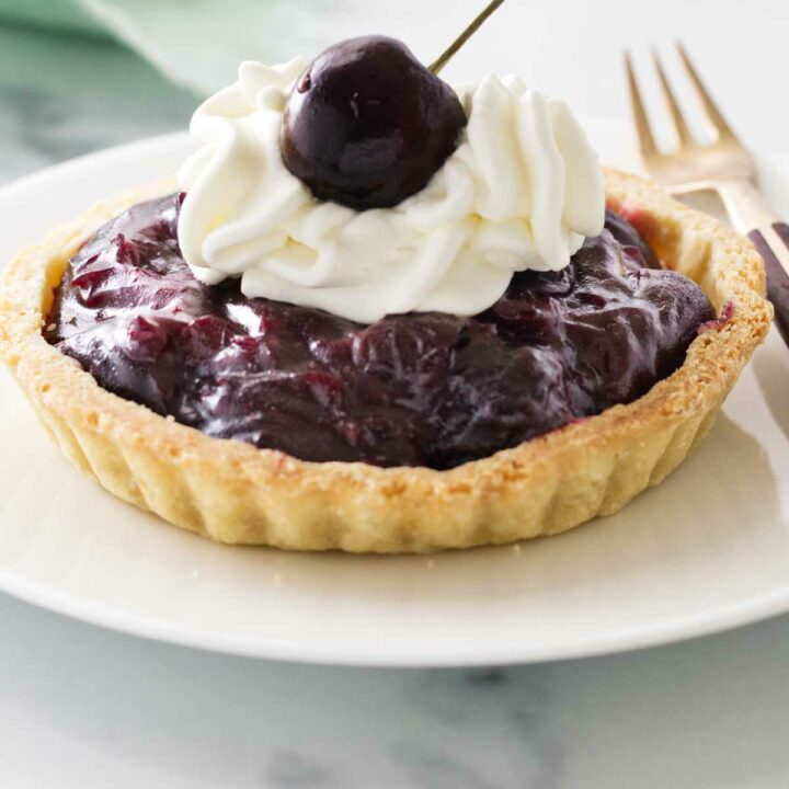 a mini cherry tart on a serving plate with a fork.