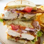 A plate with a chicken bacon ranch sandwich, cut in half and stacked. Potato chips