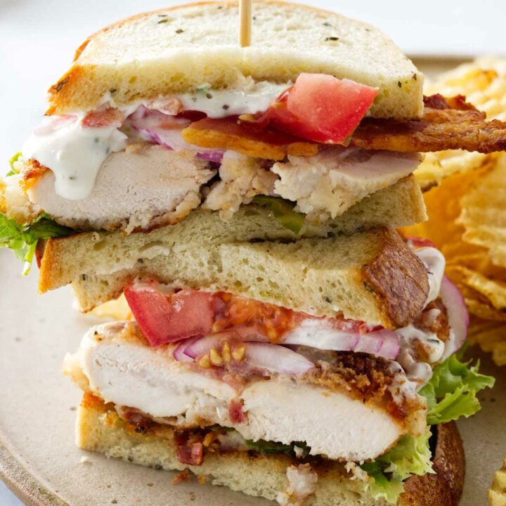 A plate with a chicken bacon ranch sandwich, cut in half and stacked. Potato chips