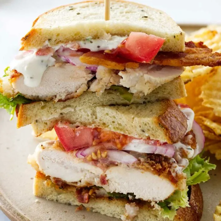 A plate with a chicken bacon ranch sandwich, cut in half and stacked. Potato chips
