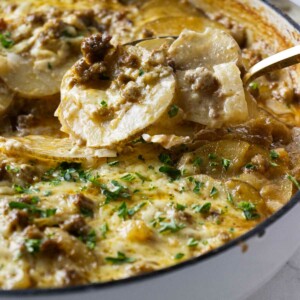 Scooping a serving of hamburger potato casserole from a skillet.