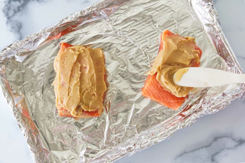 Spreading miso-butter on two portions of salmon.