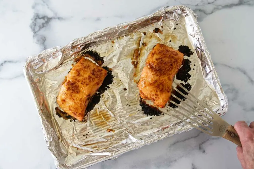 Removing the baked miso butter salmon from the baking sheet with a spatula.