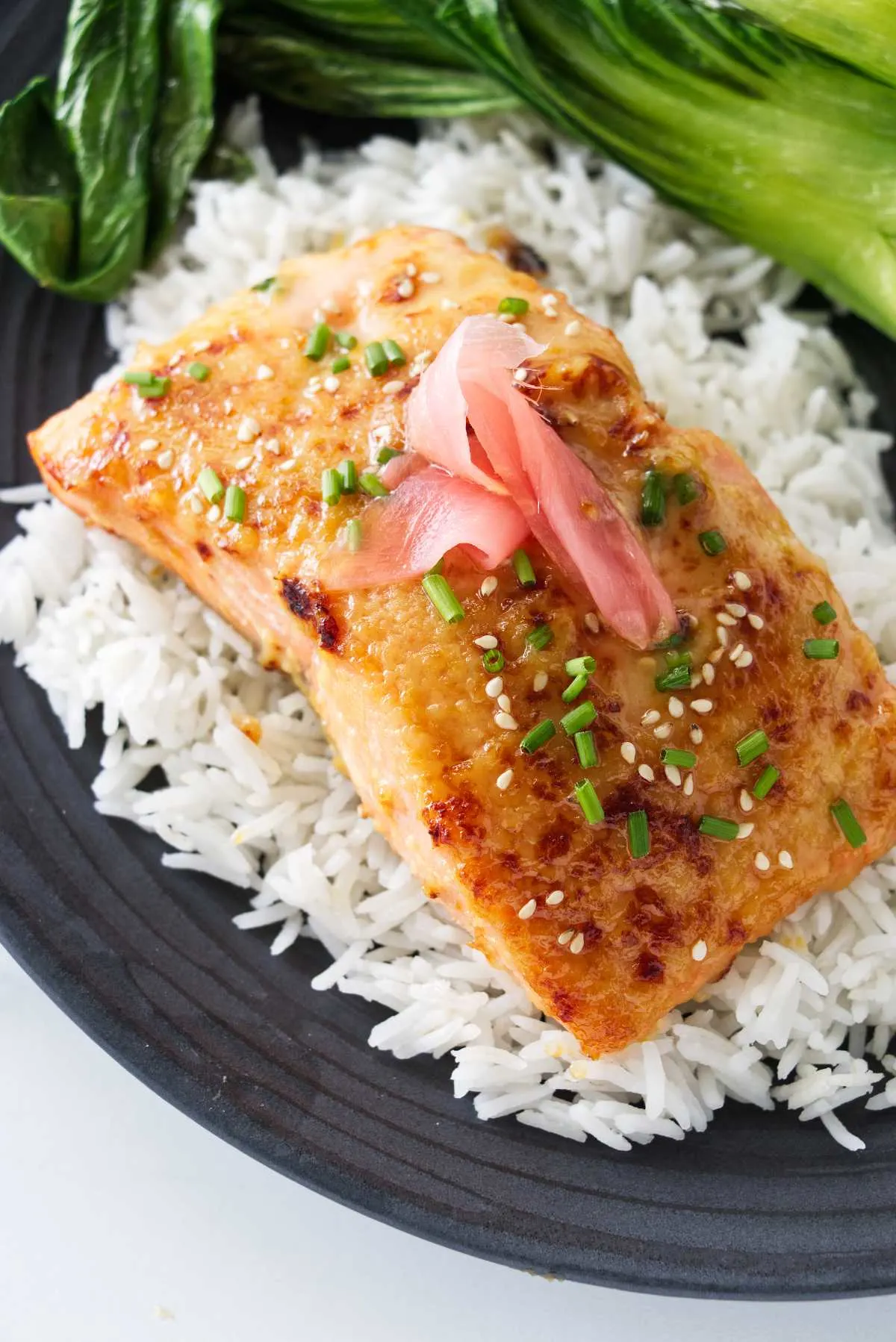 A plated serving of miso butter salmon on a mound of jasmine rice, baby bok choy on the plate next to the rice.