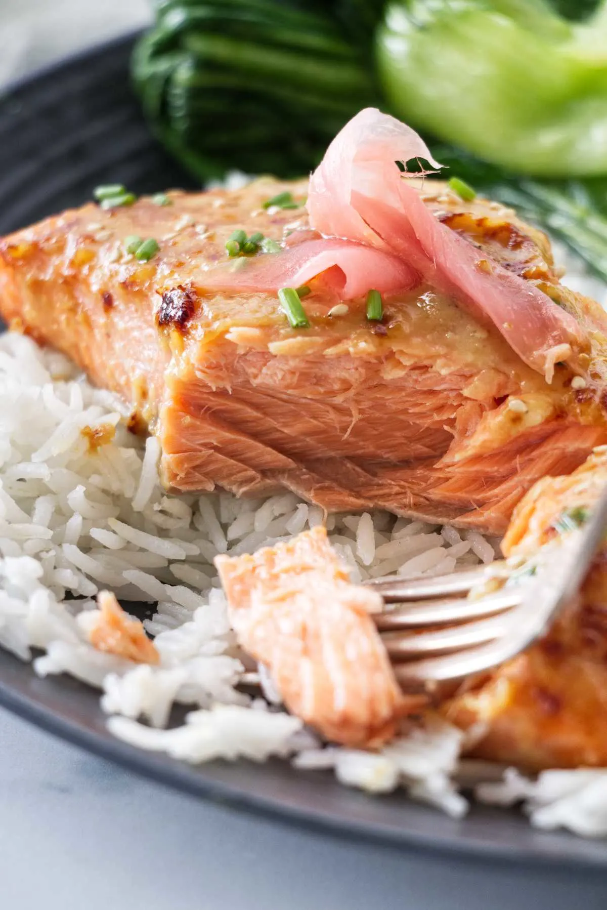 A close up view of a plated serving of miso butter salmon and a fork with a bite of salmon.
