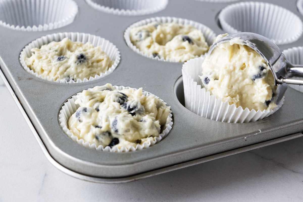 Scooping blueberry sourdough muffin batter into muffin tins.