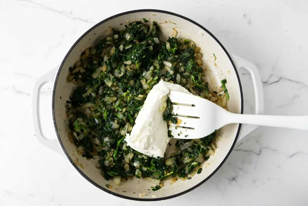 Adding cream cheese to the sautéed spinach.