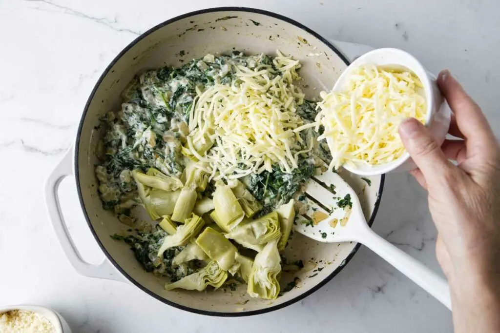 Adding cheese and artichokes to the skillet.