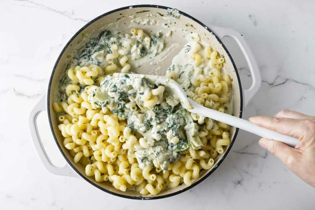 Folding pasta into the artichoke spinach mixture.