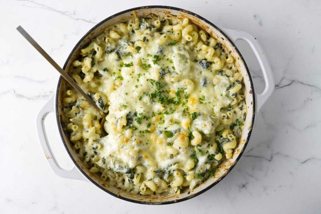 A spoon in a hot casserole loaded with spinach, artichokes, and pasta.
