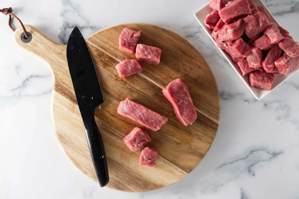NY Steak on a cutting board with a knife, being cut into bite size pieces. A plate of steak bites on the side.