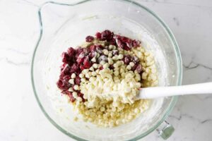 Folding strawberries and white chocolate chips into muffin batter.