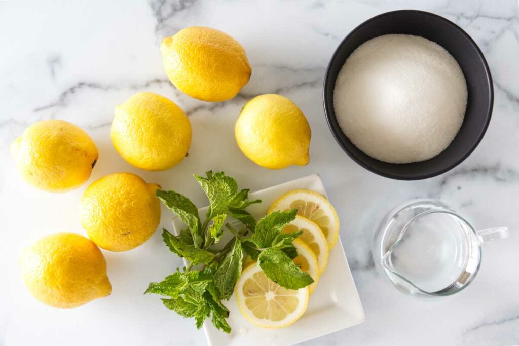Ingredients to make old fashioned lemonade: lemons, sugar and water. A small plate with lemon slices and fresh mint.