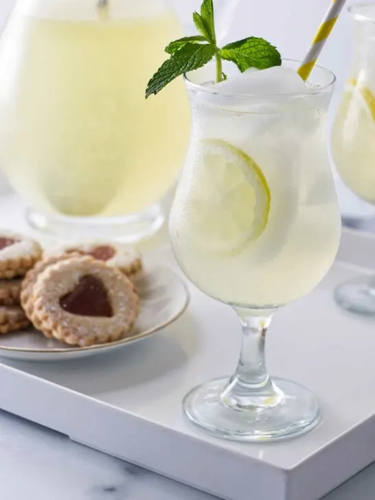 A tray with glasses of old fashioned lemonade garnished with fresh mint, a pitcher of lemonade and a plate of cookies.