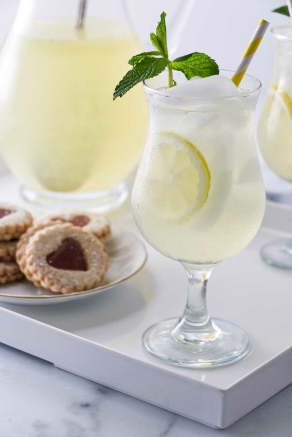 A tray with glasses of old fashioned lemonade garnished with fresh mint, a pitcher of lemonade and a plate of cookies.