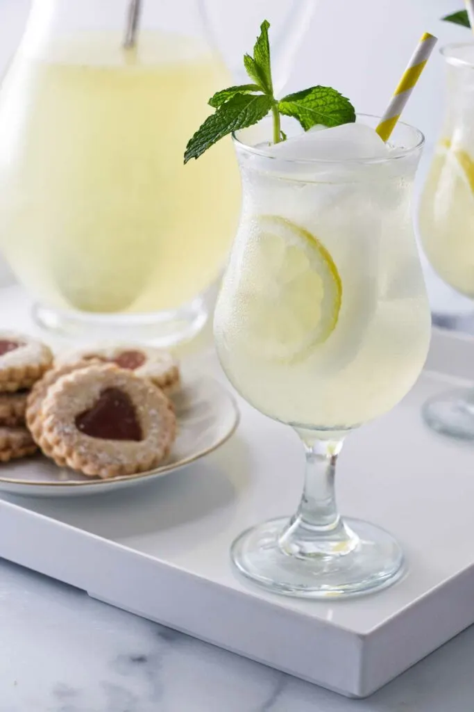 A tray with glasses of old fashioned lemonade garnished with fresh mint, a pitcher of lemonade and a plate of cookies.