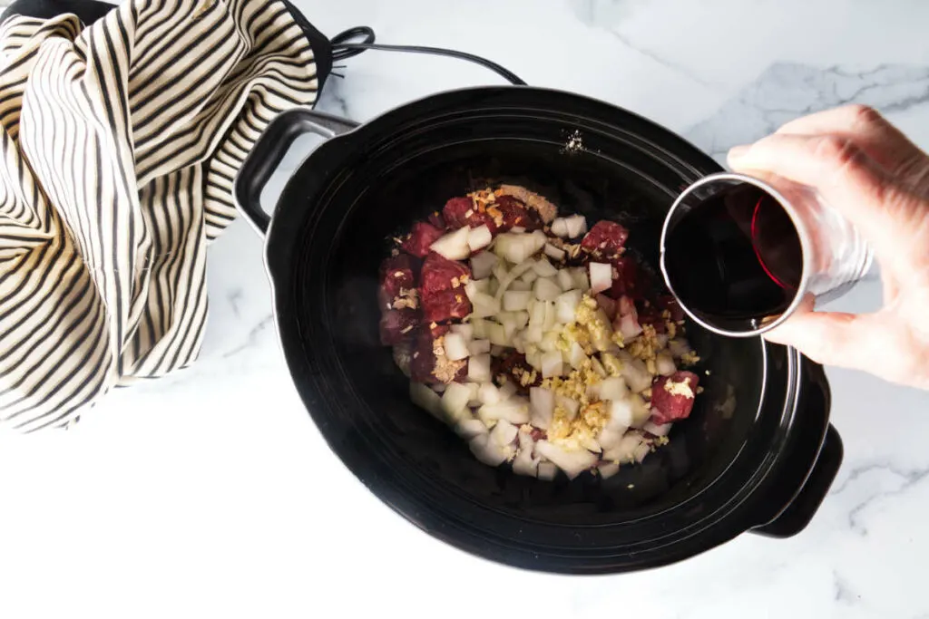 Pouring red wine into a slow cooker of vegetables.