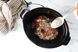 Spooning tapioca over stew meat and onions in a slow cooker.