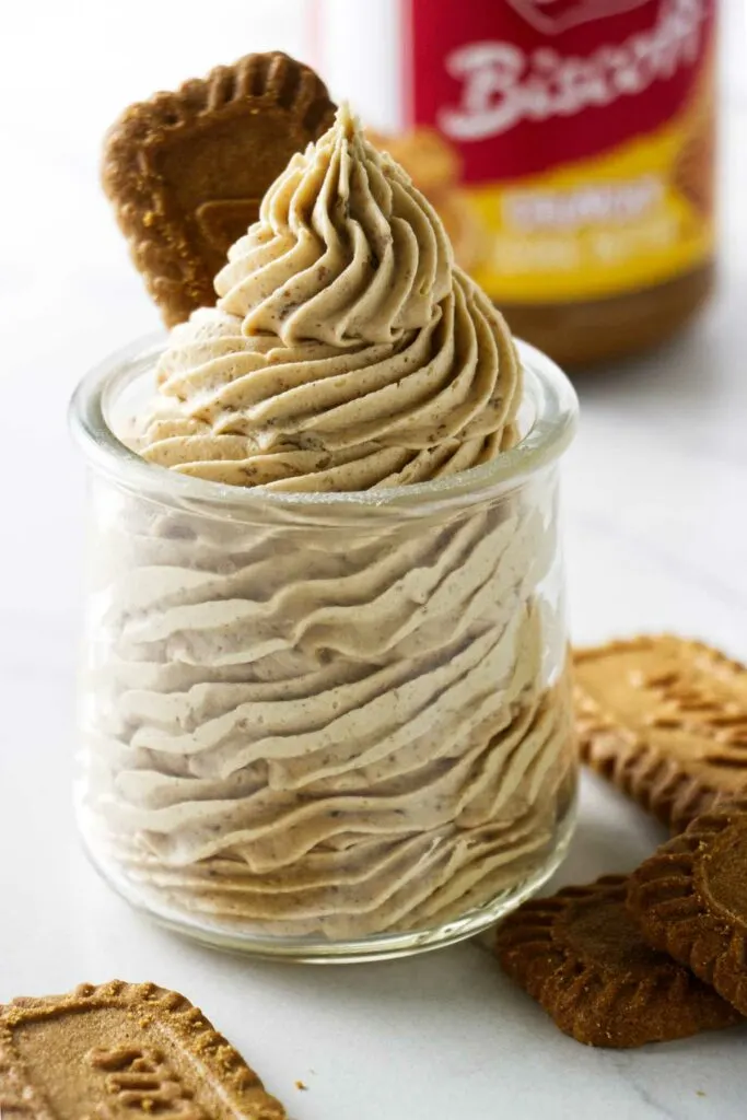 A jar piped with a swirl of biscoff buttercream next to biscoff cookies.