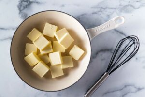 A skillet with slices of butter and a wire whisk next to the skillet.