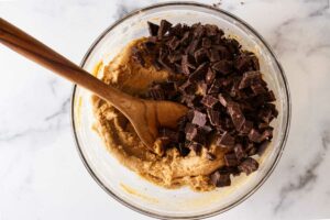 A bowl of cookie dough, chunks of chocolate and a wooden spoon.