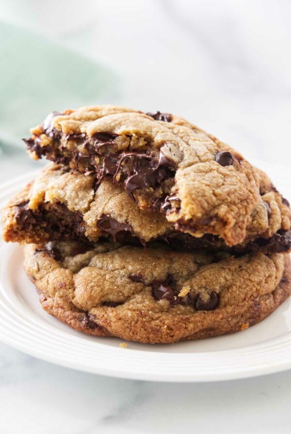 Two cookies on a plate, one cookie broken in half and stacked on the whole cookie.