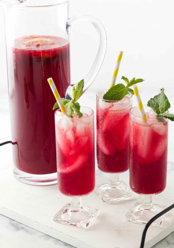 A serving tray with a pitcher filled with a red beverage and three glasses of red iced lemonade infused with hibiscus.